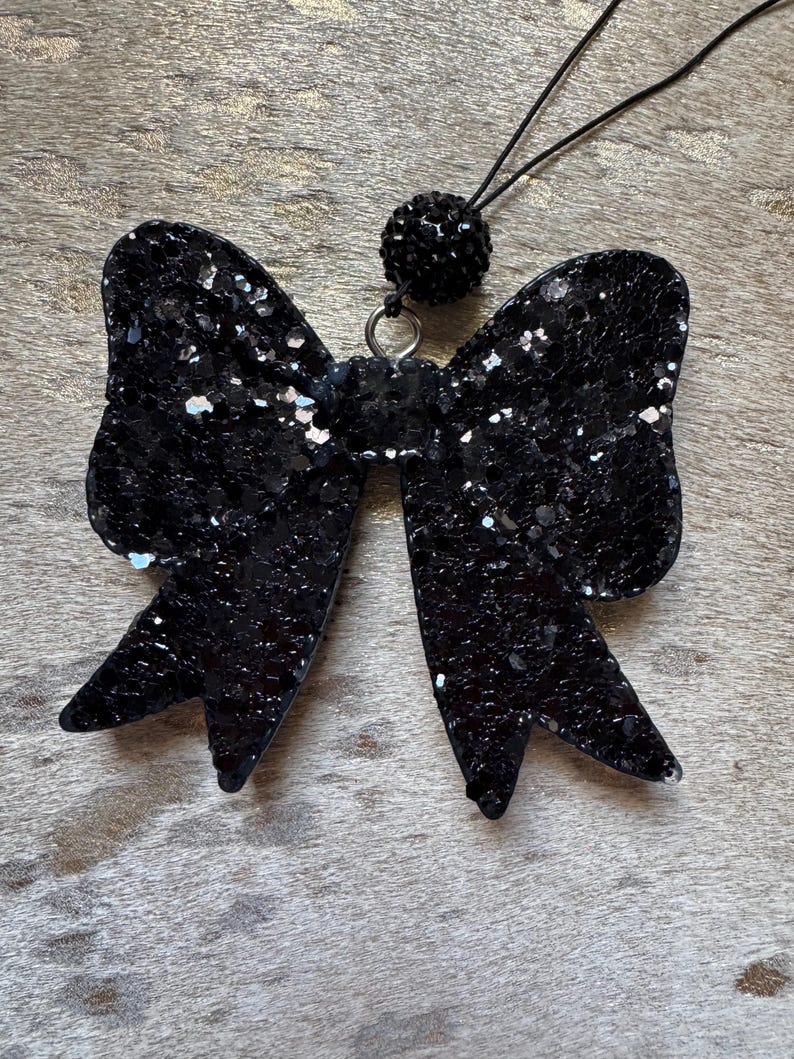Peut inclure: Un n&oelig;ud en paillettes noires avec un accent en strass noir sur une ficelle noire.