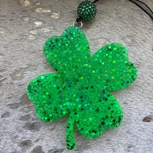 May include: A green glitter four-leaf clover charm with a black string and a green rhinestone bead.