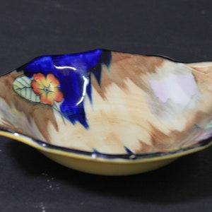 May include: A small, scalloped ceramic bowl with a brown, yellow, blue and pink floral design. The bowl has a ruffled edge and a glossy finish.