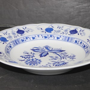 Puede incluir: Un tazón de sopa de cerámica blanca con un patrón floral azul. El tazón tiene un borde festoneado y un borde ligeramente elevado.