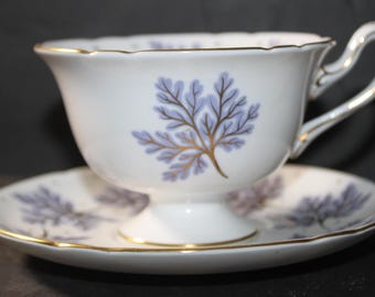 Può includere: Un set da tè bianco con bordo dorato e un motivo a felce blu e oro.