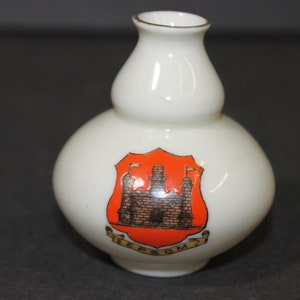May include: A white ceramic vase with a double gourd shape. It features a red and gold crest with a castle and the text "Iffley" on a white background.