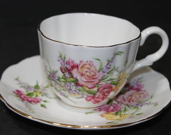 May include: A white teacup and saucer set with a floral design featuring pink, yellow, and purple flowers. The set has a gold trim around the edges.