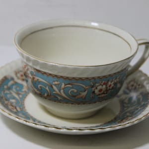 May include: A white teacup and saucer with a blue and gold floral pattern. The cup has a gold rim and the saucer has a scalloped edge.