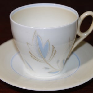 May include: A white teacup and saucer with a blue and gold leaf design.