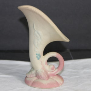 Peut inclure: Un vase en céramique vintage en forme de corne avec un glaçage rose et blanc. Le vase présente un motif floral en bleu et blanc.