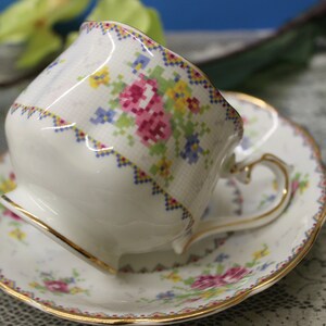 May include: A white teacup and saucer with a floral pattern in shades of pink, yellow, and blue. The cup and saucer have a gold trim.