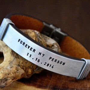 Può includere: Un braccialetto in pelle marrone con una fascia argentata incisa con il testo "Forever My Person 11.16.2014".