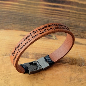 May include: Brown leather bracelet with a metal clasp. The bracelet has the text "For God so loved the world that he gave his only begotten Son, that whoever believes in him shall not perish but have everlasting life." engraved on it.
