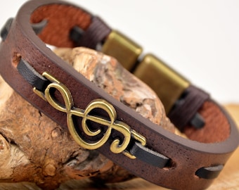 May include: A brown leather bracelet with a black leather accent and a gold treble clef charm.