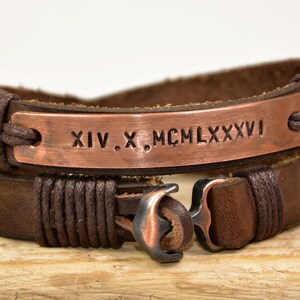 Puede incluir: Un brazalete de cuero marr&oacute;n con un dije de ancla de cobre y una placa de cobre grabada con los n&uacute;meros romanos XIV. X. MCM LXXXVI.