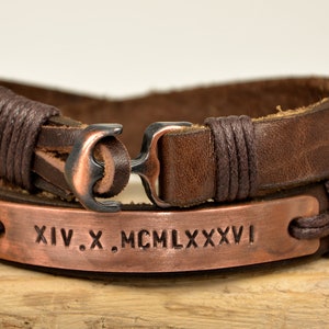 Puede incluir: Pulsera de cuero marr&oacute;n con un dije de ancla de cobre y una placa de cobre grabada con los n&uacute;meros romanos XIV.X. MCM LXXXVI.