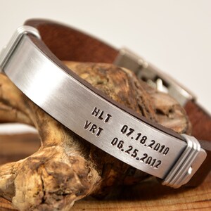 May include: A brown leather bracelet with a silver metal band engraved with the text "HLT 07.18.2010 VRT 06.25.2012".