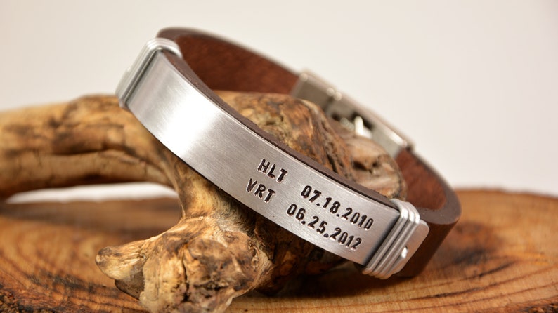 May include: A brown leather bracelet with a silver metal band engraved with the text "HLT 07.18.2010 VRT 06.25.2012".