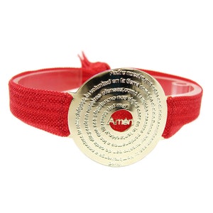 May include: Red elastic bracelet with a gold-toned round charm featuring the Lord's Prayer in Spanish. The charm has a red center with the word "Amen" in white.