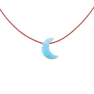May include: A delicate crescent moon pendant necklace with a blue opal stone, hanging from a red string.