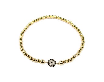 May include: A gold beaded bracelet with a small evil eye charm. The charm is set with clear and black stones.