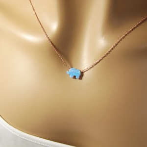 May include: A delicate gold chain necklace with a small blue opal elephant pendant.