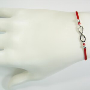 May include: Red string bracelet with a silver infinity symbol charm and silver beads.