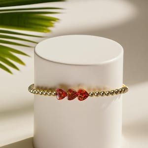 May include: A gold beaded bracelet with three red heart-shaped opal charms.