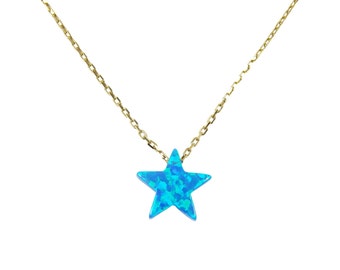 May include: A gold-colored chain necklace with a blue star-shaped pendant. The star has a textured, opalescent appearance, with shades of blue and turquoise. The necklace is displayed against a white background.