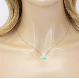May include: A delicate gold chain necklace with a small, light green opal pendant shaped like a Christmas tree.