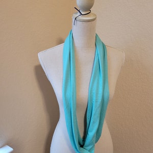 May include: A turquoise infinity scarf displayed on a white mannequin.