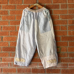 May include: Wide-leg pants featuring a patchwork design with light blue, white, and navy blue stripes and solid panels. The pants have an elasticized waistband, two side pockets, and decorative horizontal yellow and white stitched accents at the hem.