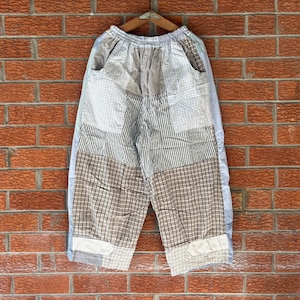May include: Wide-leg trousers featuring a patchwork design with various patterns including brown and white plaid, thin vertical stripes, and solid light blue panels. The pants have an elasticized waistband and side pockets, constructed from multiple fabric segments.