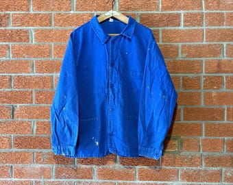 May include: A bright blue long-sleeve work jacket featuring a classic collar, a button-down front closure, and two large lower patch pockets. The fabric displays visible white paint splatters and signs of wear throughout the garment.