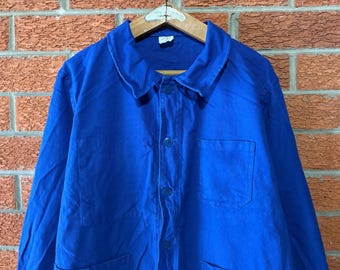 May include: A vibrant blue long-sleeve work jacket featuring a classic collar, a front button-down closure with matching blue buttons, and a single chest pocket on the left side. The garment is constructed from a durable, solid-colored fabric.
