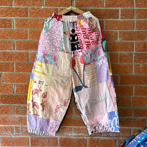Puede incluir: Pantalones anchos con diseño de patchwork que incluye varios patrones como estampados florales, rayas y texto gráfico. La tela muestra múltiples colores como rosa, azul, amarillo y blanco, con ilustraciones de conejos y cerezas.