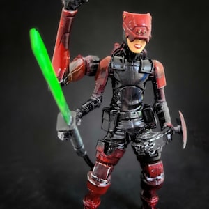 May include: A detailed action figure of a futuristic warrior in black and red armor, holding a green lightsaber and a small axe. The figure has a red helmet and a raised hand with a green gem. The text "ROBOT RESURRECTION" is at the bottom.