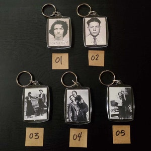 May include: A collection of five clear acrylic keychains. Each keychain features a vintage black and white photograph or mugshot. The keychains have silver-colored metal rings. The images include portraits and group photos.