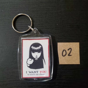 May include: A clear acrylic keyring with a rectangular insert showing a black and white illustration of a girl pointing. The text "I WANT YOU to leave me alone" is below the image. A metal keyring is attached.