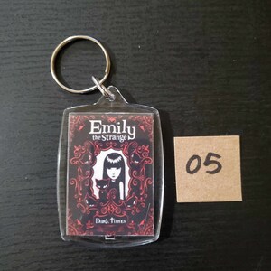 May include: Clear acrylic keychain with an "Emily the Strange" graphic. The rectangular keychain has a silver metal ring. The graphic is a black and red design with the text "Emily the Strange" and "Dark Times".