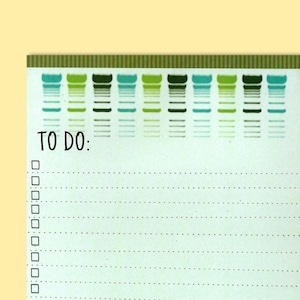 May include: A green and white to-do list notepad with a decorative border of green, blue, and white stripes. The notepad has a section for writing "TO DO:" and a checklist with blank lines.