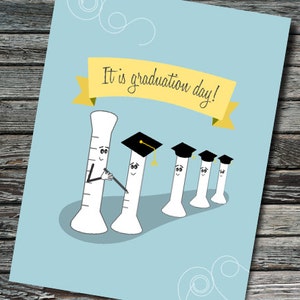 May include: A graduation card with a light blue background and a yellow banner that says "It is graduation day!"  The card features a cartoon illustration of a graduated measuring cylinder with a cap and gown, handing a diploma to another measuring cylinder.