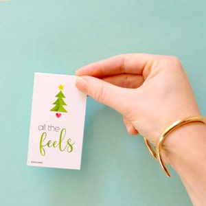 May include: A white card with a green watercolor Christmas tree with a yellow star on top and a red heart at the base. The text on the card reads "all the feels".