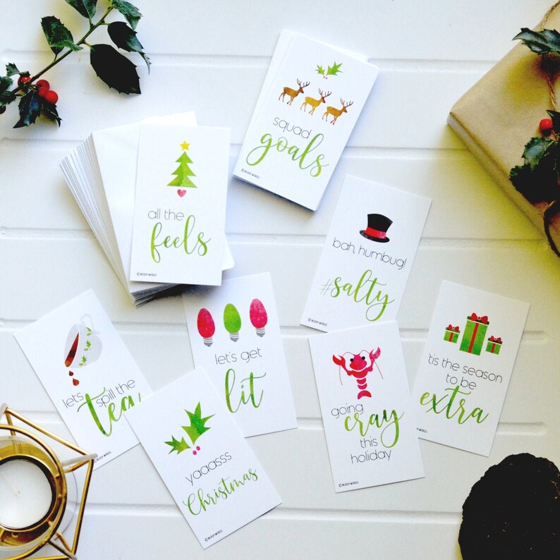 May include: A set of ten Christmas-themed gift tags with various illustrations and phrases, including "all the feels", "squad goals", "bah humbug! #salty", "let's get lit", "yaaasss Christmas", "lets spill the tea", "going cray this holiday", and "tis the season to be extra".