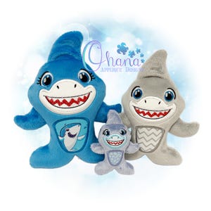 Puede incluir: Tres juguetes de peluche de tiburón de diferentes tamaños. El más grande es azul con un diseño de tiburón. El tiburón mediano es gris y el más pequeño es azul claro. Todos tienen bocas sonrientes con dientes rojos y ojos azules.