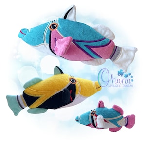 May include: Three plush toy fish in different sizes and colors. The largest fish is turquoise, pink, and white. The middle fish is yellow, black, and green. The smallest fish is turquoise, pink, and white. The fish are all smiling and have big eyes. The text "Ghana Applique Designs" is visible in the background.