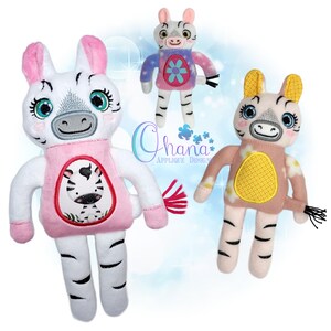 May include: Three plush zebra dolls with embroidered details. The zebras have white bodies with black stripes, pink or yellow accents, and smiling faces. One doll has a pink shirt with a zebra design, and the others have flower designs. The text "Ohana Applique Design" is visible.