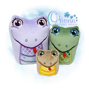 May include: Three plush snake toys in shades of purple, green, and tan. Each snake has large, expressive eyes, a smiling mouth, and a decorative pattern on its body. The text "Ohana Applique Designs" is visible.