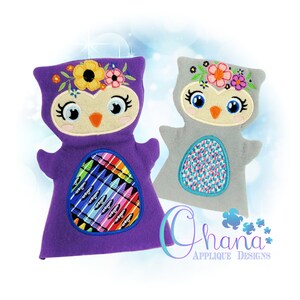 May include: Two purple and gray owl hand puppets with embroidered details. The purple owl has a pocket on its chest with a colorful crayon design. The gray owl has a blue and white geometric design on its chest. Both owls have flowers on their heads.