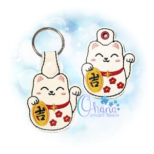 May include: White embroidered lucky cat keychain with a red collar and a gold coin with the Chinese character "福" (Fu) for good fortune.