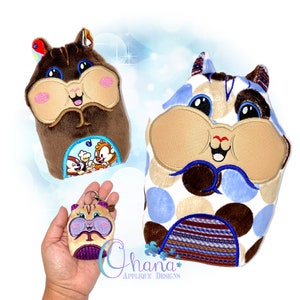 May include: Three plush toys in the shape of a hamster. The largest hamster is brown and white with blue polka dots. The medium-sized hamster is brown with a blue and white scene on its belly. The smallest hamster is purple and brown with a key ring attached.