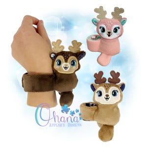 May include: A plush deer wristband in brown with a matching deer head. Two additional deer plushies in pink and brown are also shown. The deer have large blue eyes and tan antlers. The text "Ohana Applique Designs" is in the lower left corner.