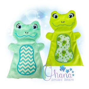 Puede incluir: Dos marionetas de rana de peluche, una verde y una azul claro. La rana verde tiene un fondo blanco con un patrón de ranas verdes más pequeñas. La rana azul claro tiene un patrón de chevron blanco y azul.