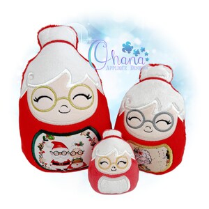 May include: Three plush Christmas ornaments in the shape of Mrs. Claus. The ornaments are red with white hair and a smiling face wearing gold-rimmed glasses. The largest ornament has a picture of Santa and Mrs. Claus.